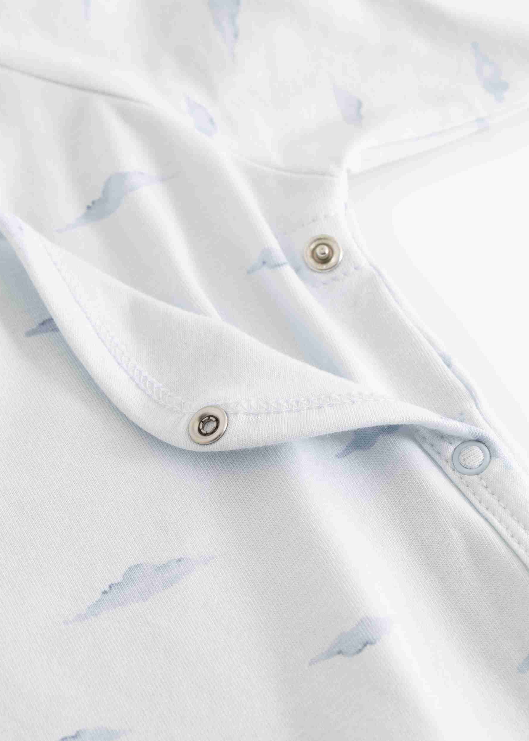 Close-up of a white baby garment with a light blue cloud print and silver metal snap buttons.
