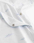Close-up of a white baby garment with a light blue cloud print and silver metal snap buttons.