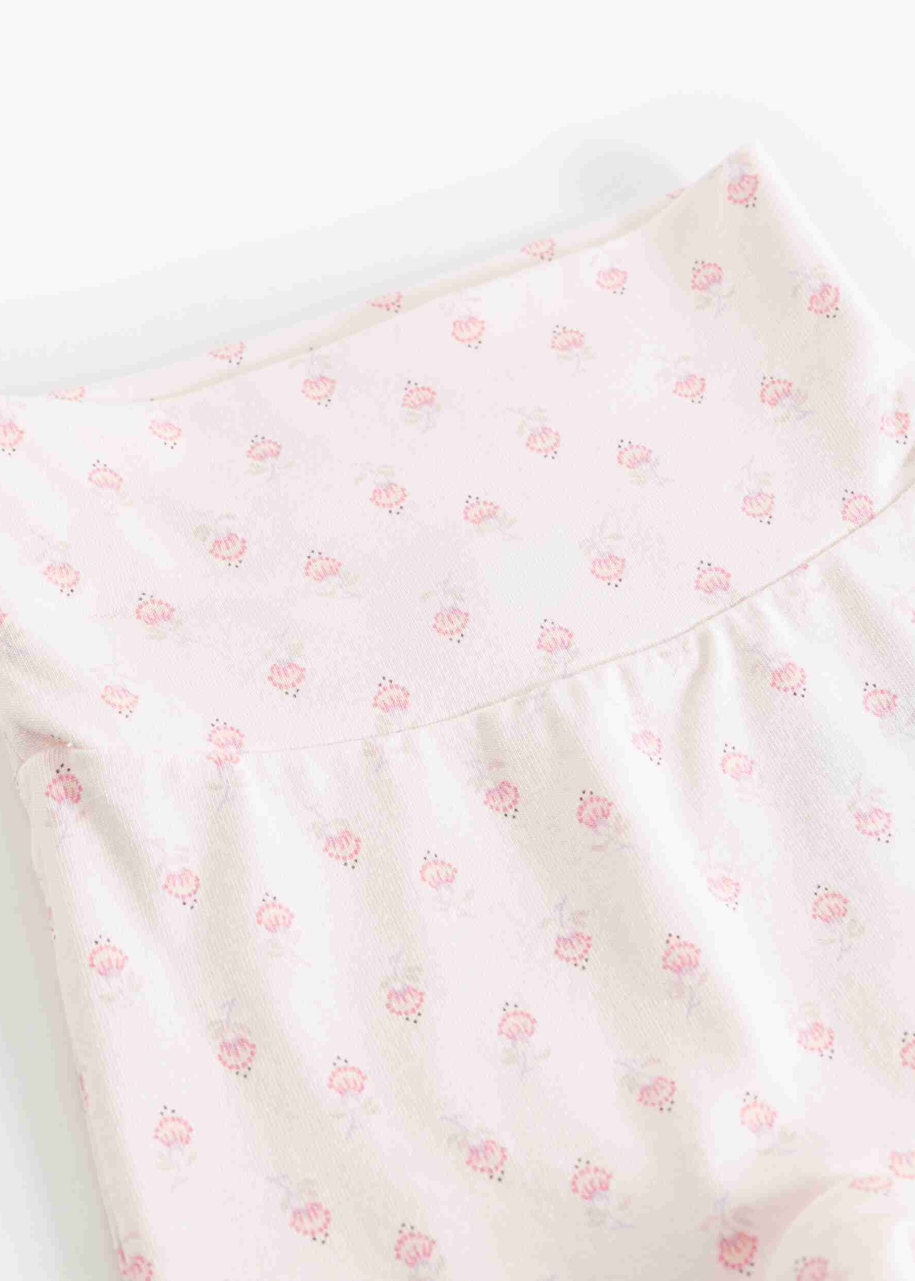A close-up of a light pink fabric garment, likely a baby romper or bodysuit, featuring a delicate repeating pattern of small pink flowers and leaves.