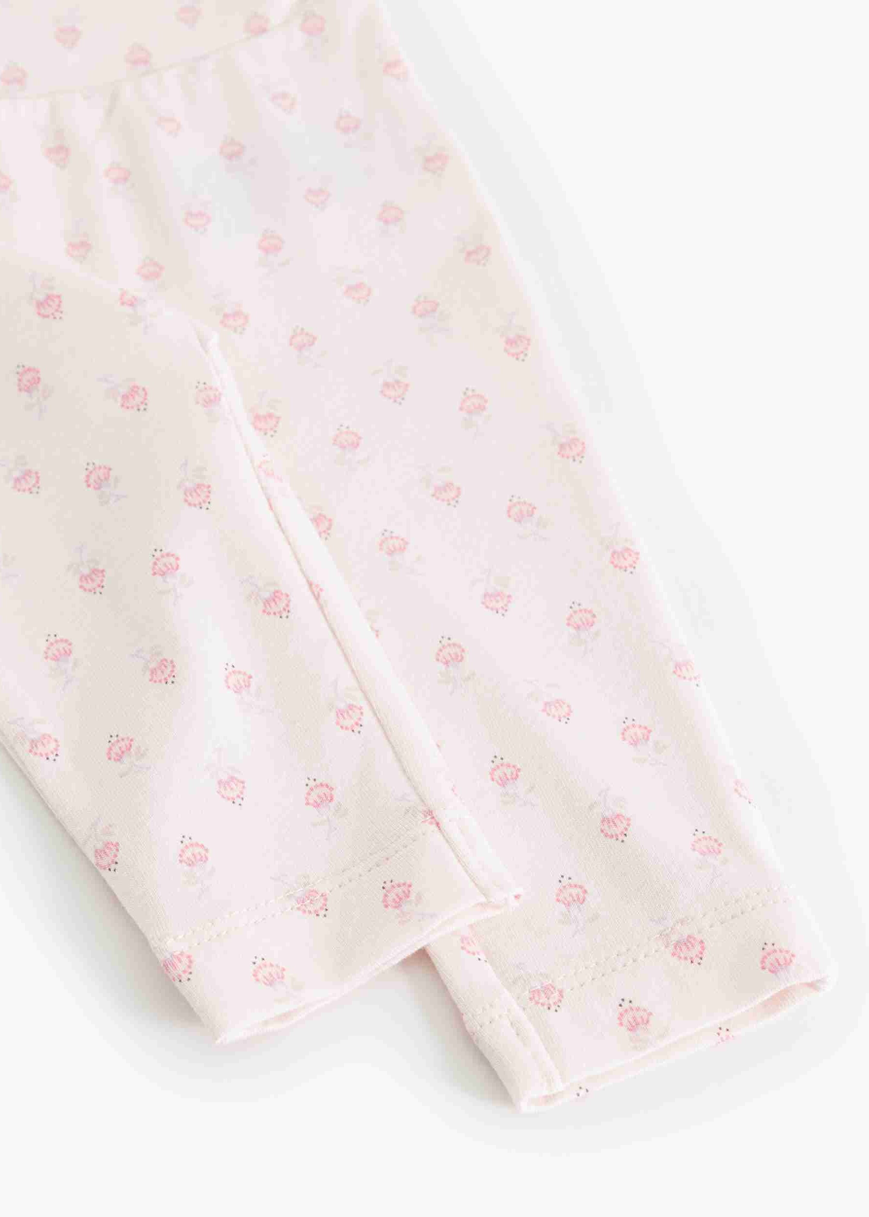 Close-up of a light pink fabric garment, likely a baby bodysuit or leggings, featuring a delicate all-over pink floral pattern and folded cuffs.