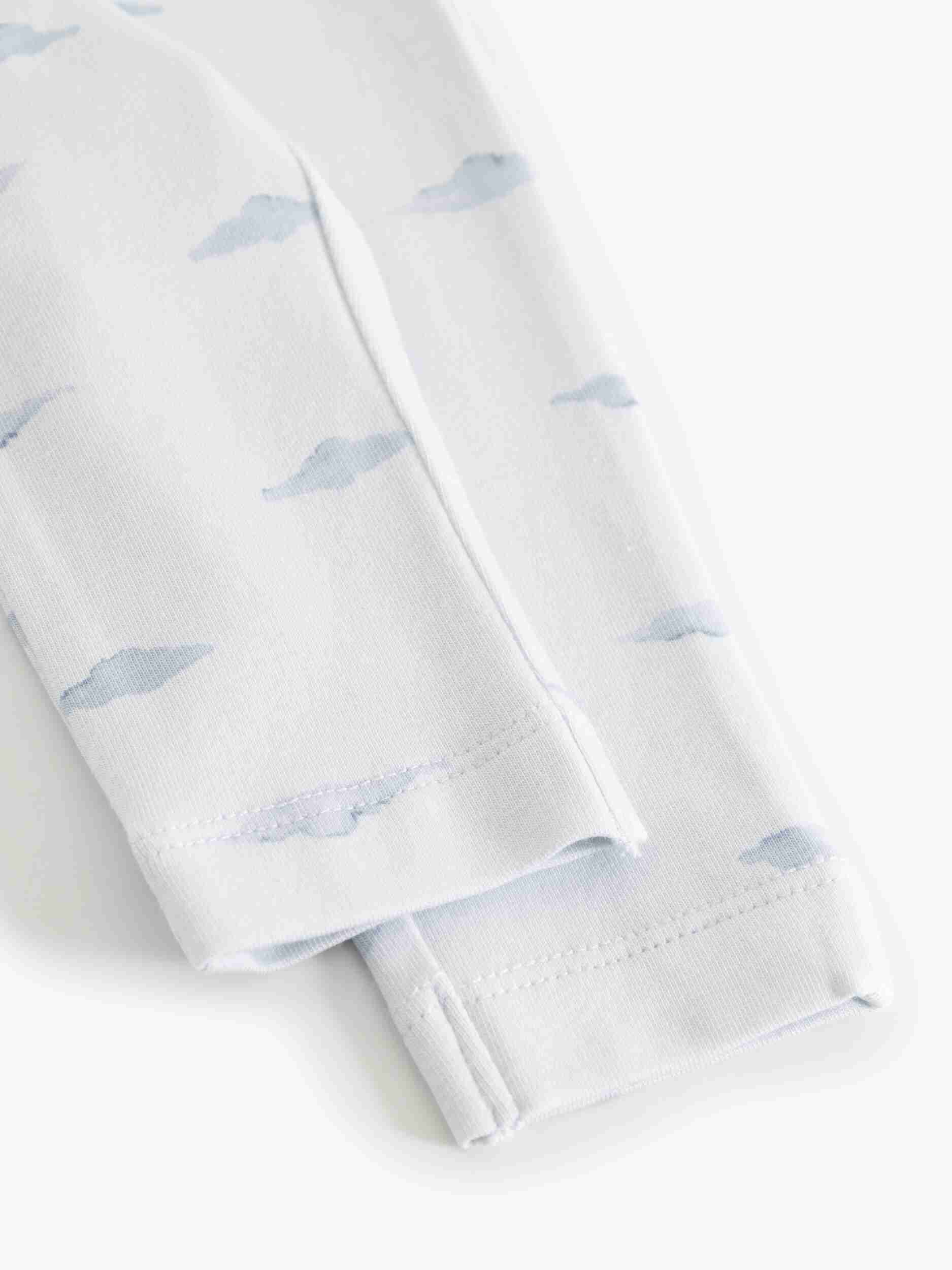 White long-sleeve baby garment, likely a sleeper or pajama, featuring a delicate light blue watercolor cloud pattern and folded cuffs.