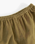 Close-up of a corduroy garment in a muted olive-brown color, showing the elastic waistband and ribbed fabric texture against a plain white background.