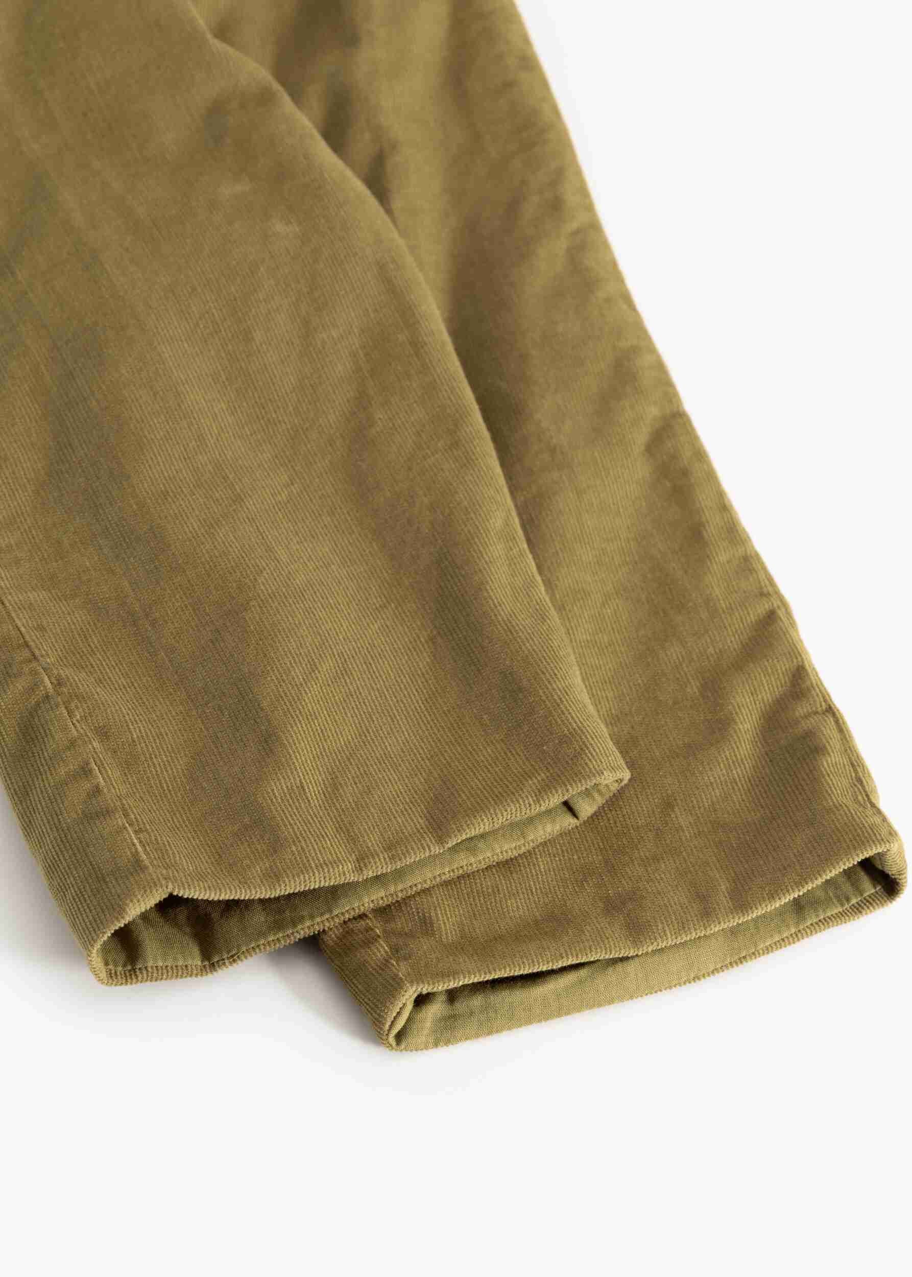 A close-up of olive green corduroy pants folded neatly on a clean white background, highlighting the textured corduroy fabric.