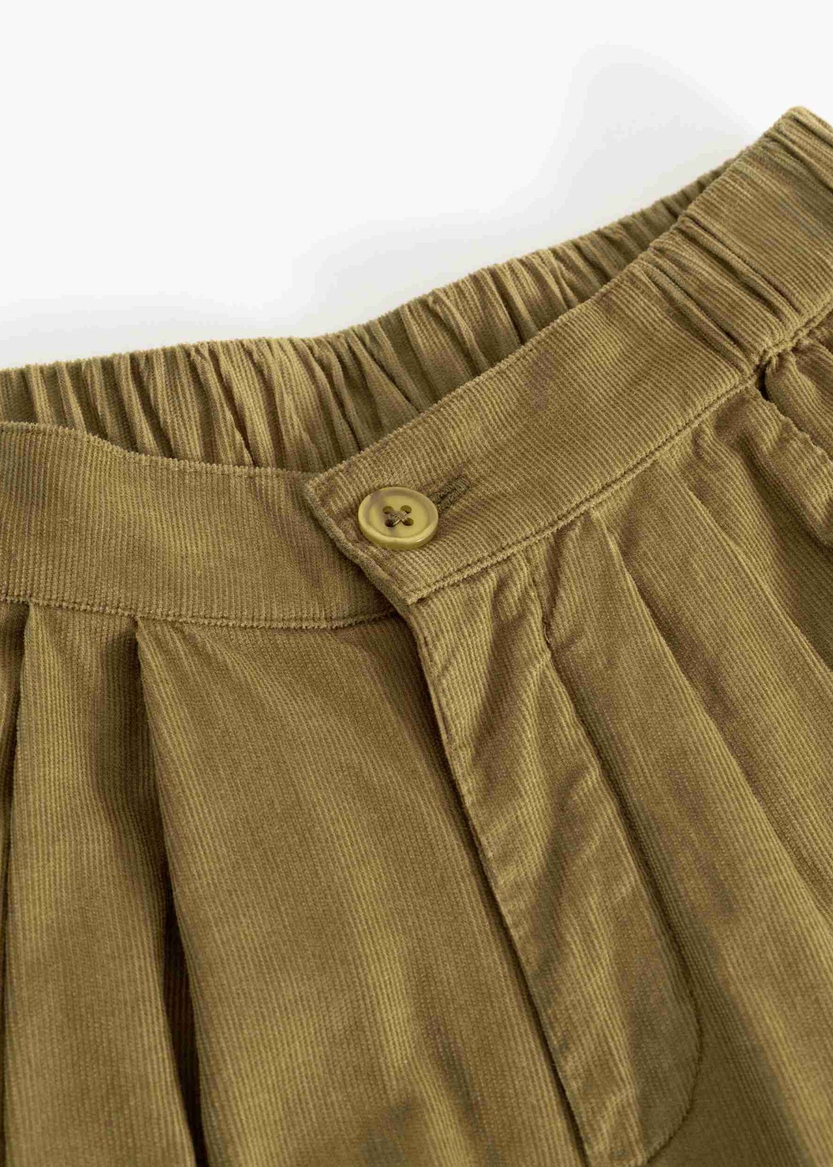 Close-up of olive brown corduroy pants showing the elastic waistband, button closure, and pleated fabric texture.