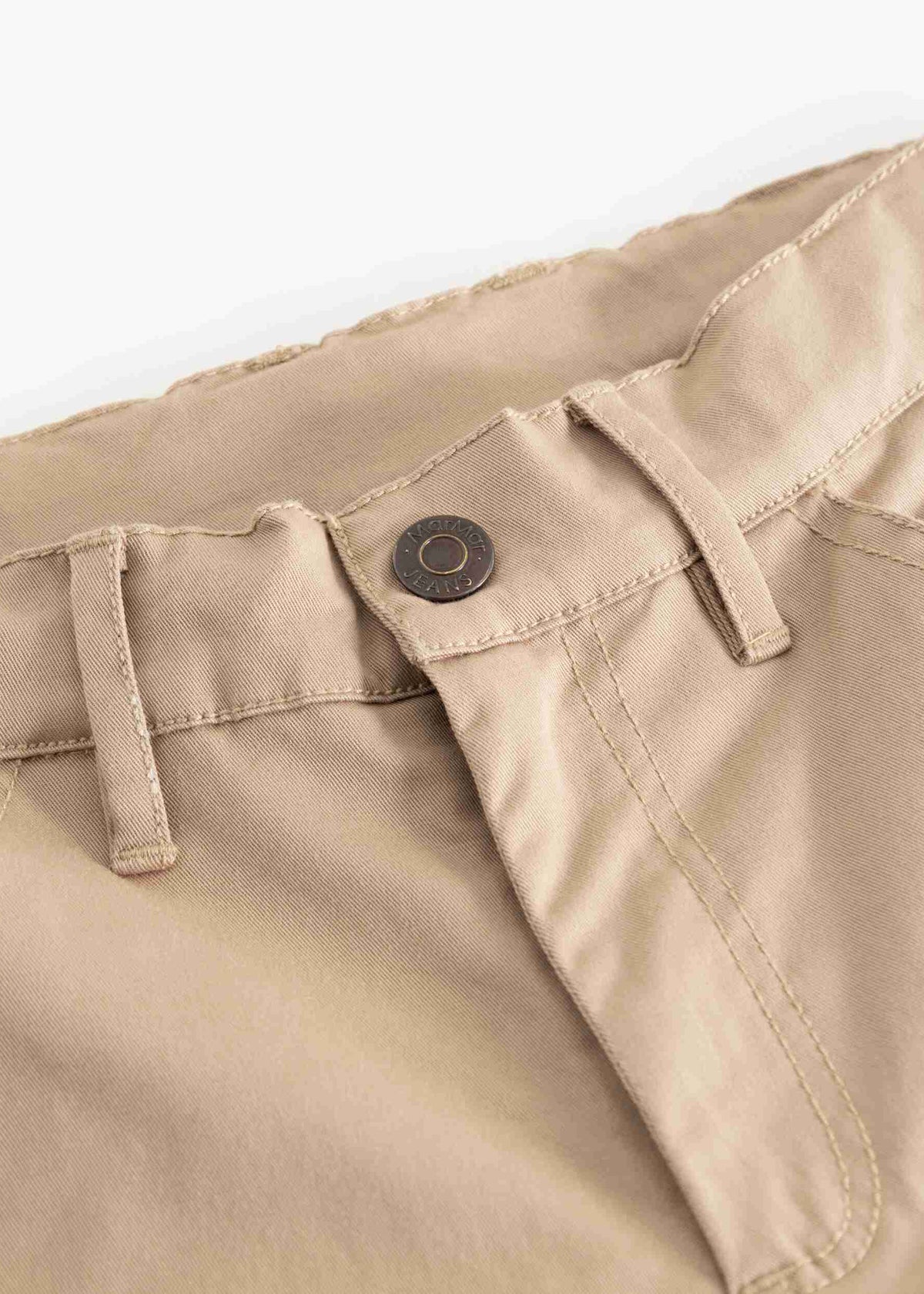 Close-up of the waistband of beige trousers, showing belt loops, a button closure, and front pocket stitching against a white background.