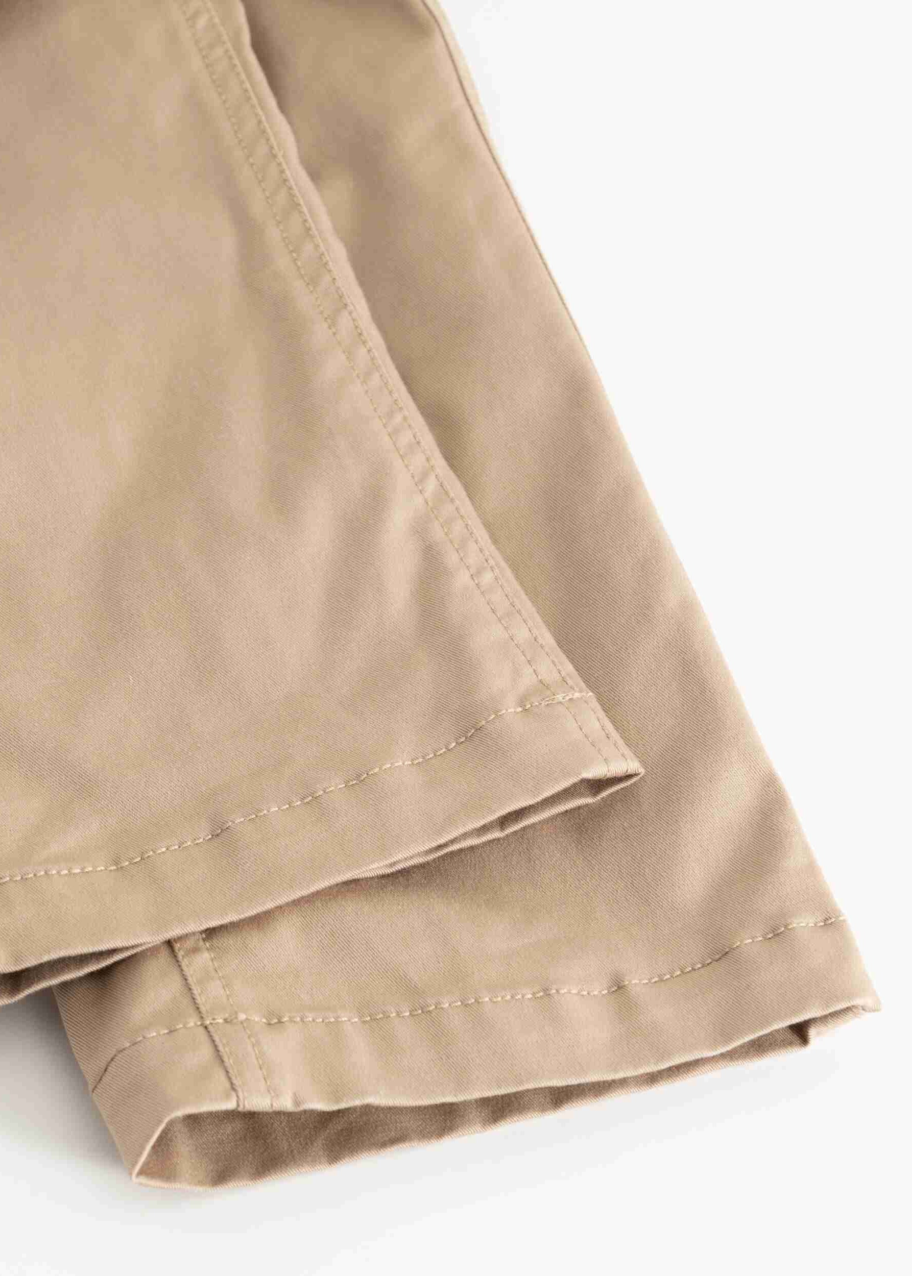 Close-up of folded khaki fabric with visible stitching and hem detail on a white background.
