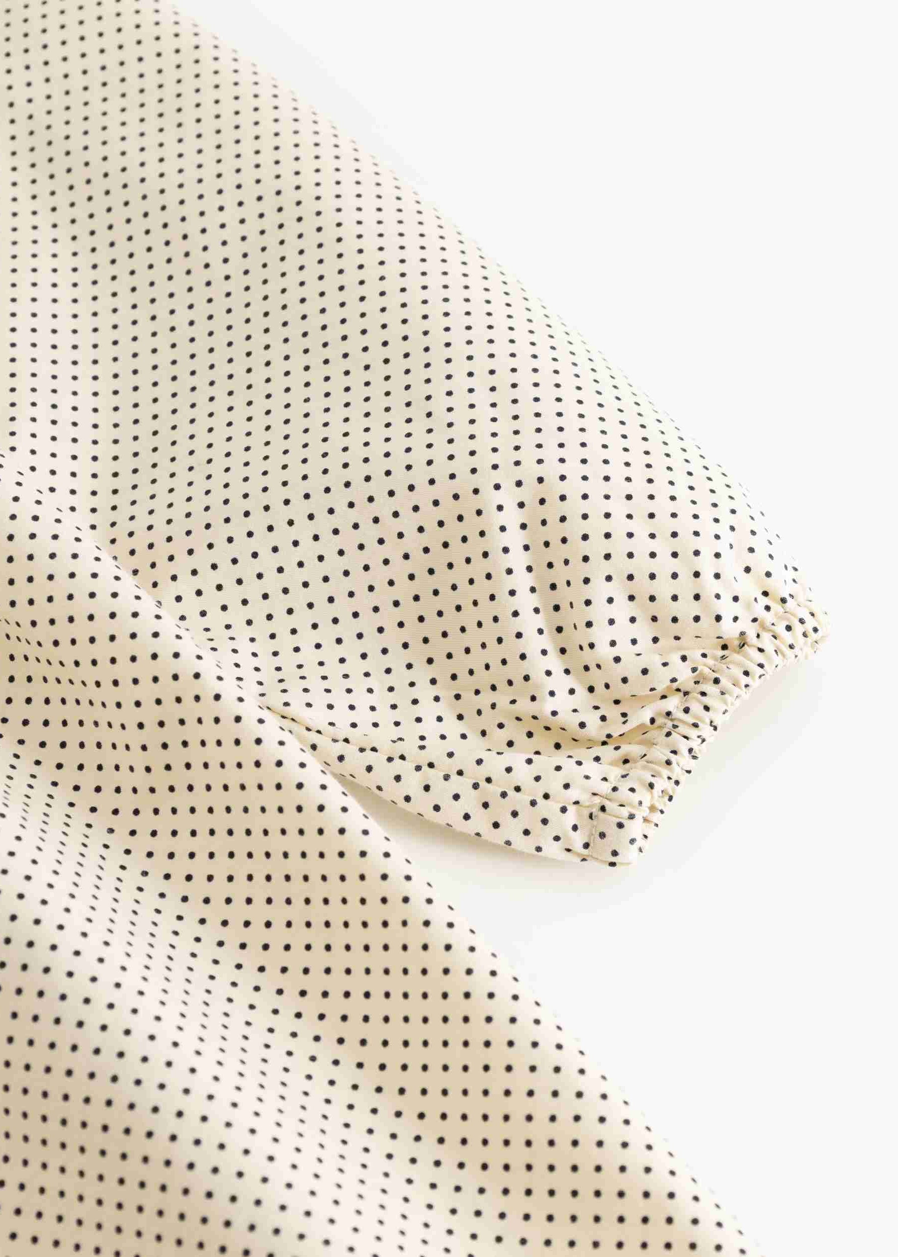 A close-up of a light beige fabric with a small black polka dot pattern, draped to show its texture and elasticized edge.