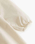 A close-up of a light beige fabric with a small black polka dot pattern, draped to show its texture and elasticized edge.