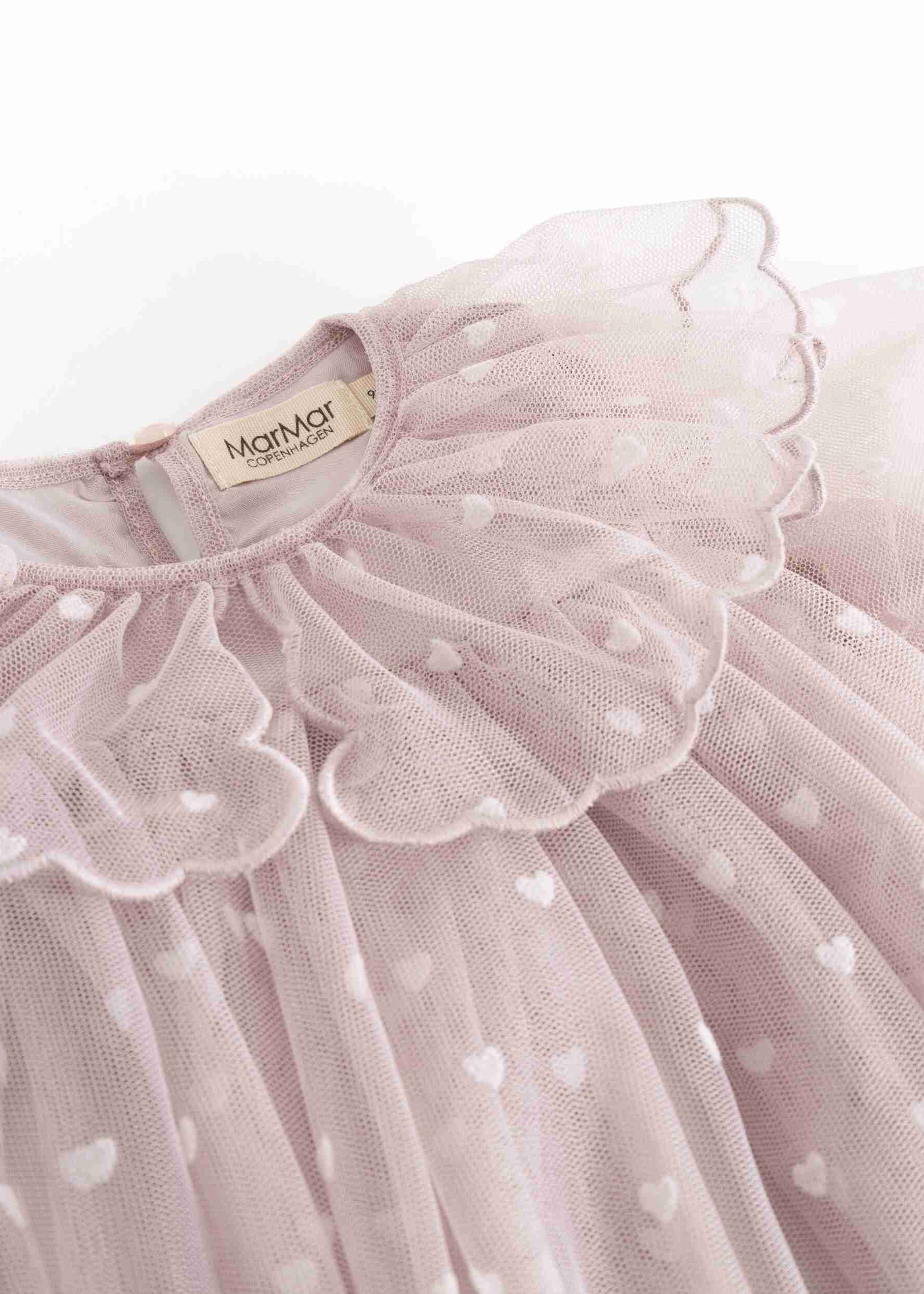 A close-up of a light pink tulle dress with a large ruffled collar and small white heart details, showing a brand label that reads 'Mamamailou'.