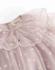 A close-up of a light pink tulle dress with a large ruffled collar and small white heart details, showing a brand label that reads 'Mamamailou'.
