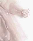 Close-up of a light pink tulle skirt with small white heart motifs and a ruffled tie detail on the sleeve, shown against a plain white background.