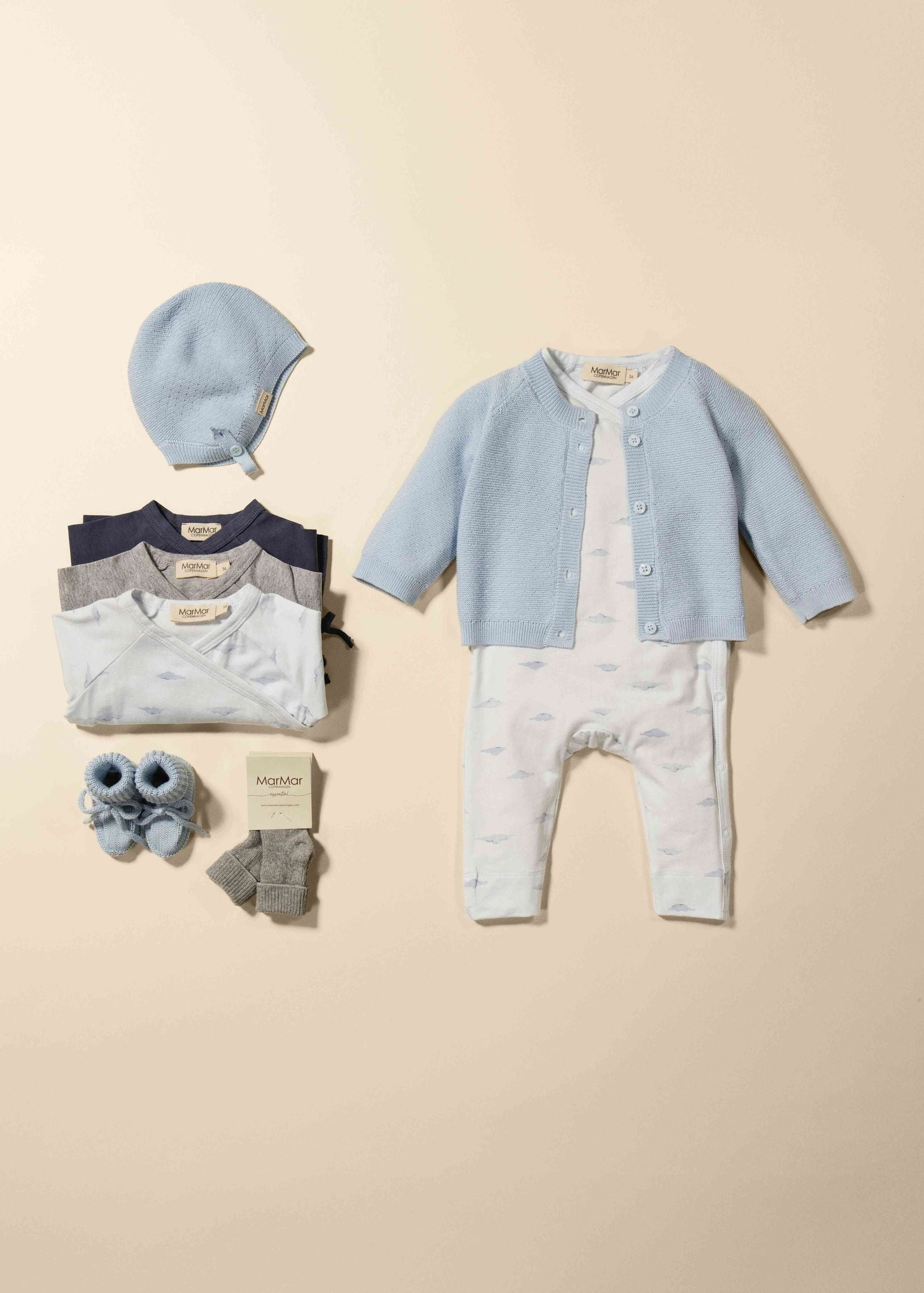Baby clothing set with cardigan, romper, hat, and socks on a beige background