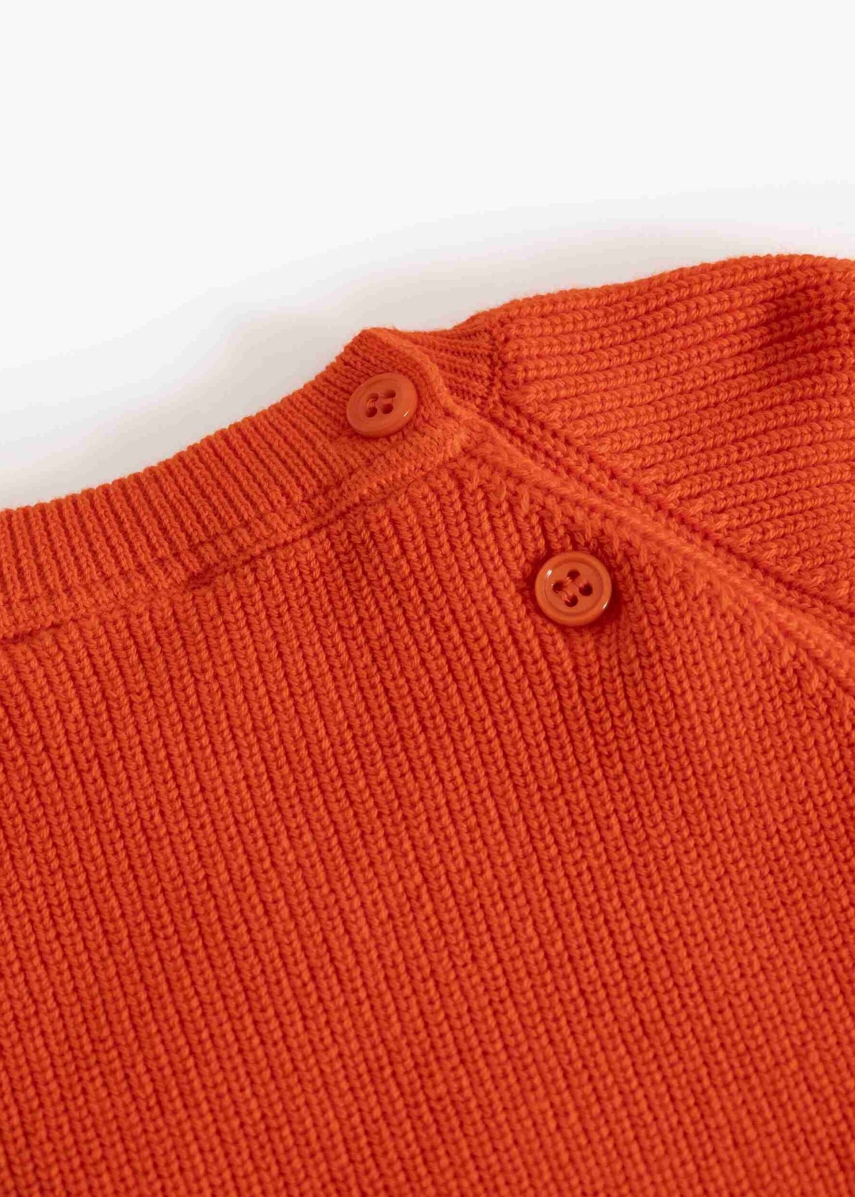 Close-up of a textured knit orange sweater with two brown buttons at the collar, set against a plain white background.