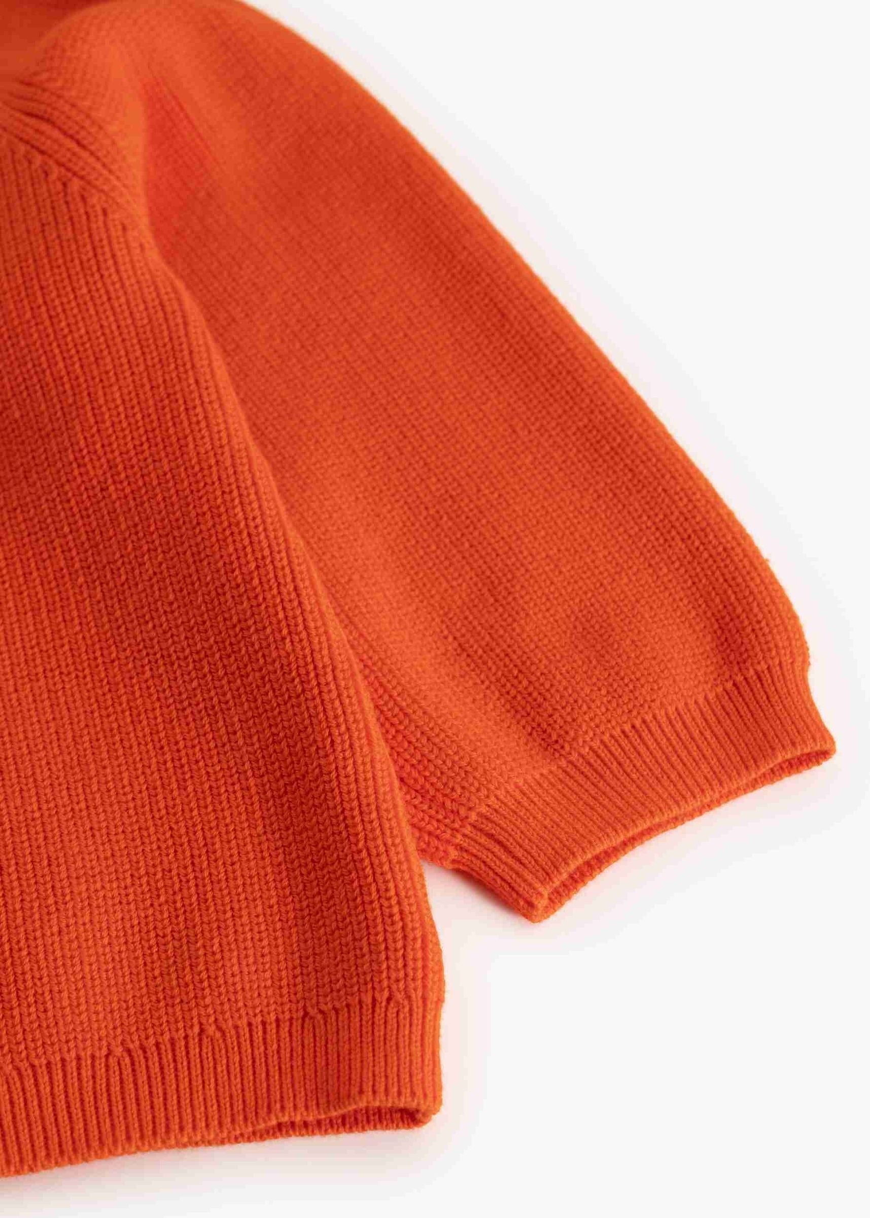Close-up of a bright orange ribbed knit garment, showing the sleeve cuff and body texture on a plain white background.