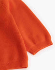 Close-up of a bright orange ribbed knit garment, showing the sleeve cuff and body texture on a plain white background.