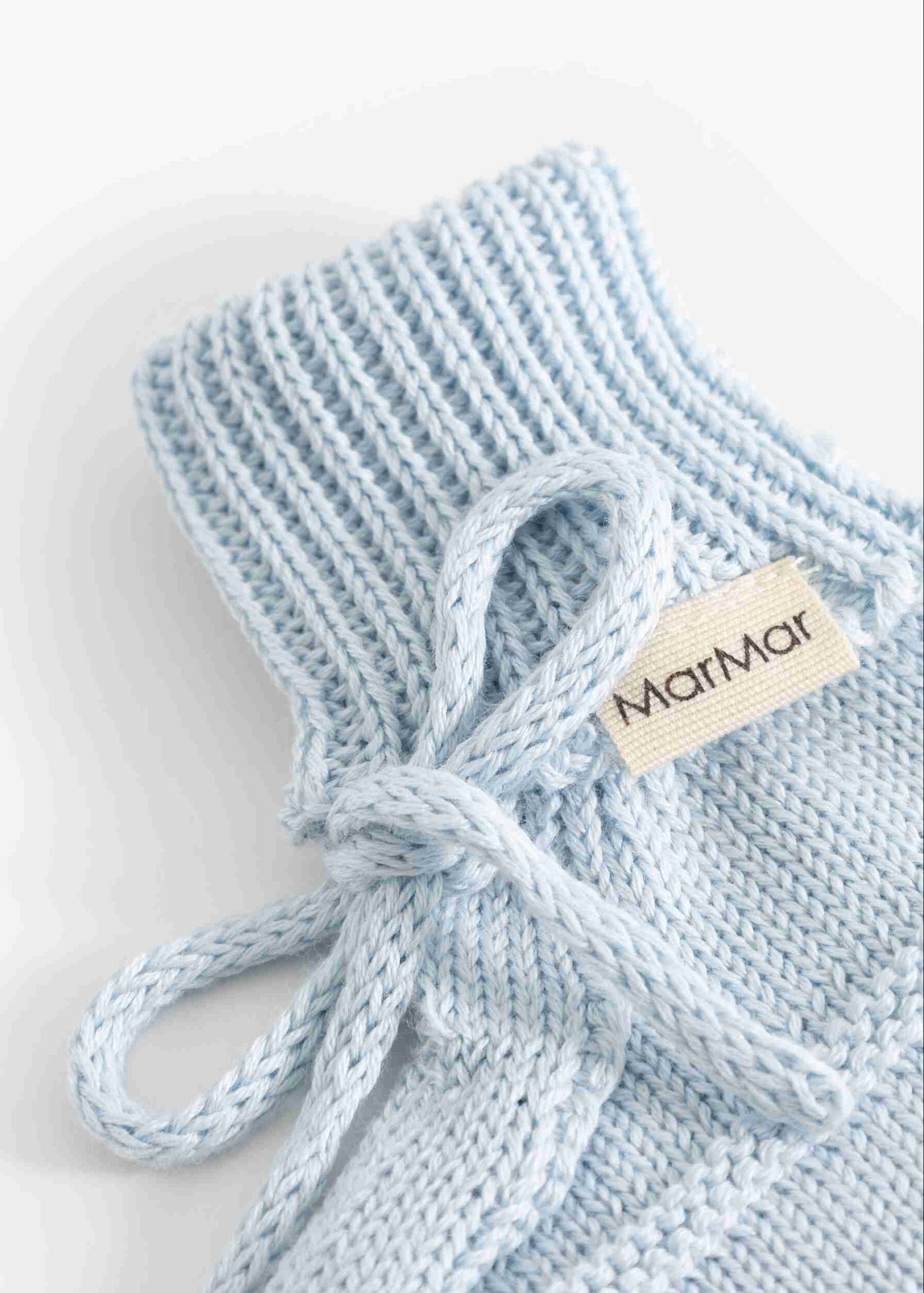 A close-up of a light blue knit baby bootie with a matching knotted tie and a beige fabric tag reading 'Mamam'.