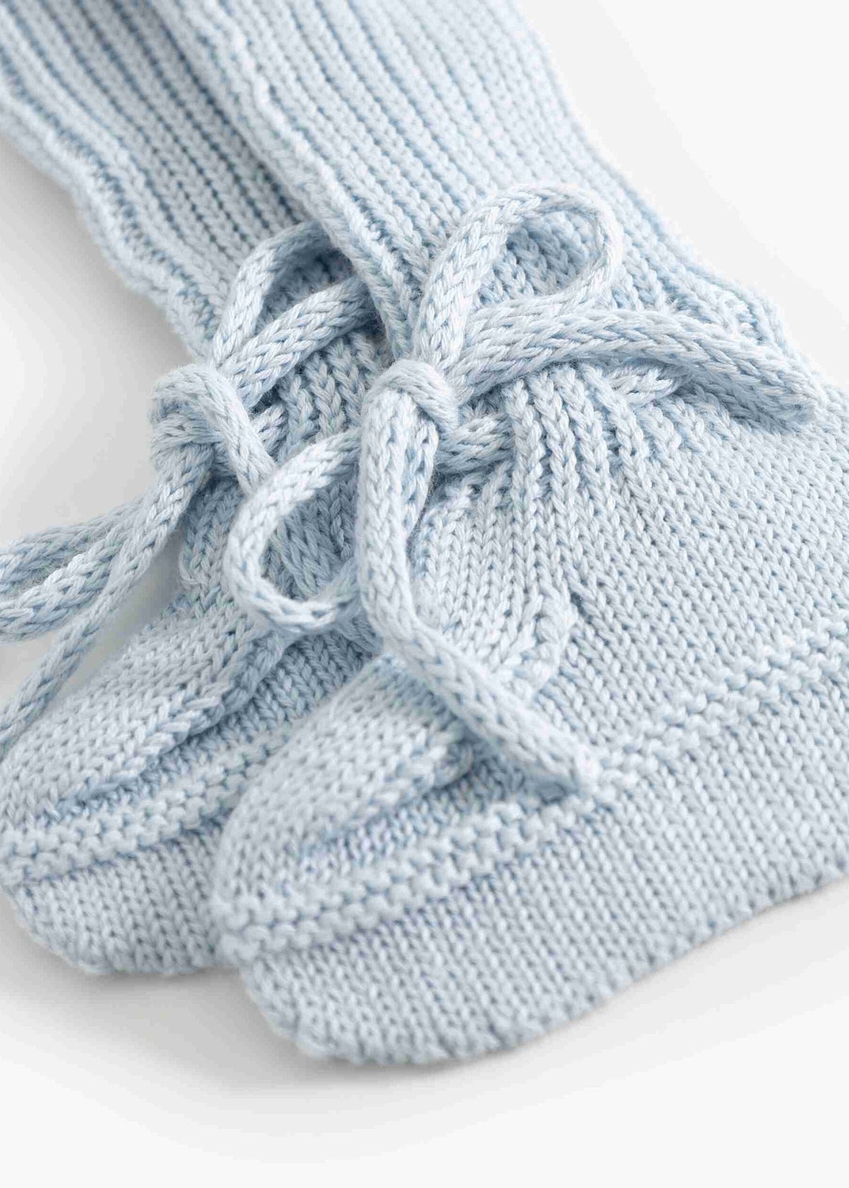 A close-up of a pair of light blue hand-knit socks with a lace-up design, shown on a clean white background.