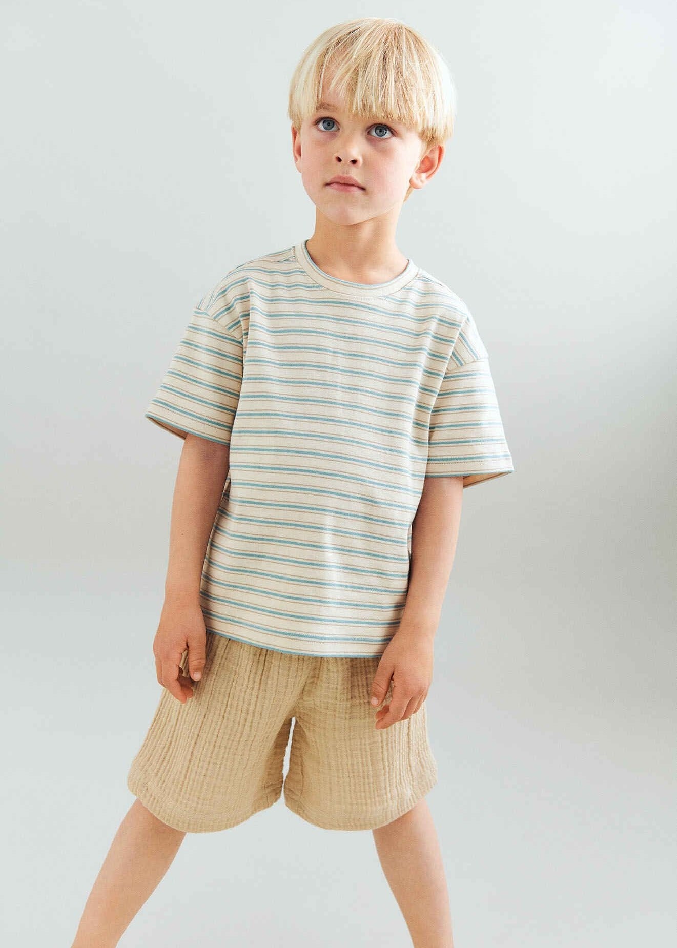 Young boy wearing a striped shirt and shorts against a plain background
