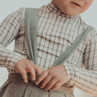 Child wearing a plaid shirt with suspenders and a neutral background