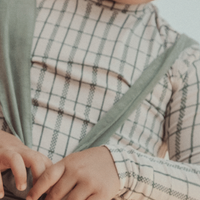 Child wearing a plaid shirt with suspenders against a neutral background