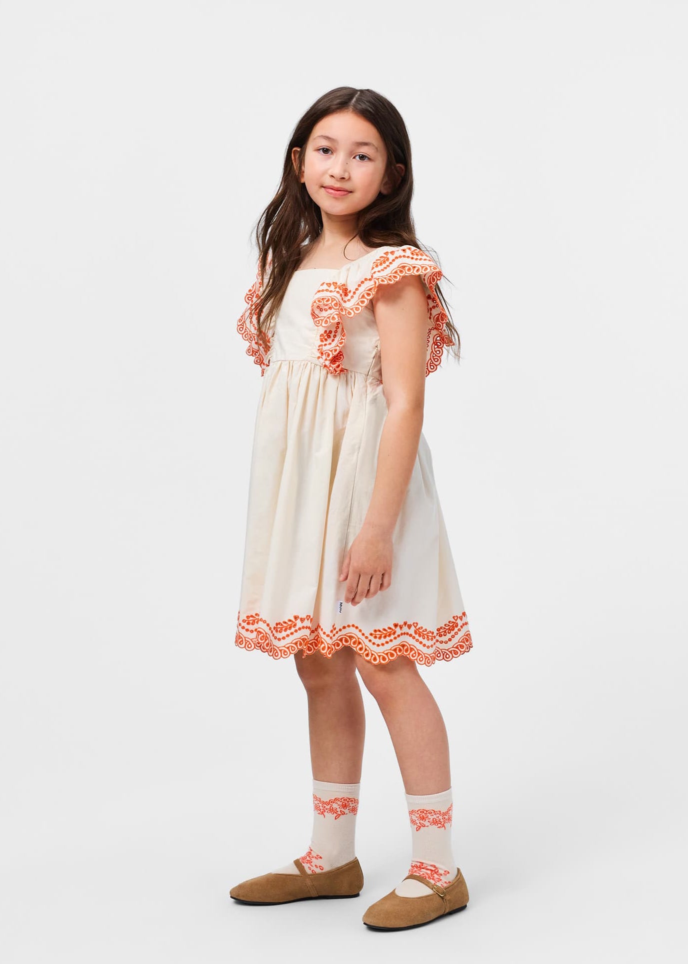 Young girl wearing a white dress with orange trim on a white background
