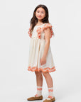 Young girl wearing a white dress with orange trim on a white background