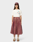 Person wearing a white t-shirt with colorful graphics, a maroon and beige striped skirt, and a maroon cap on a white background.