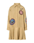 A beige long-sleeve button-up shirt dress with a pleated hem, featuring colorful embroidered patches and 'Curiosity' script on the chest, shown against a plain white background.
