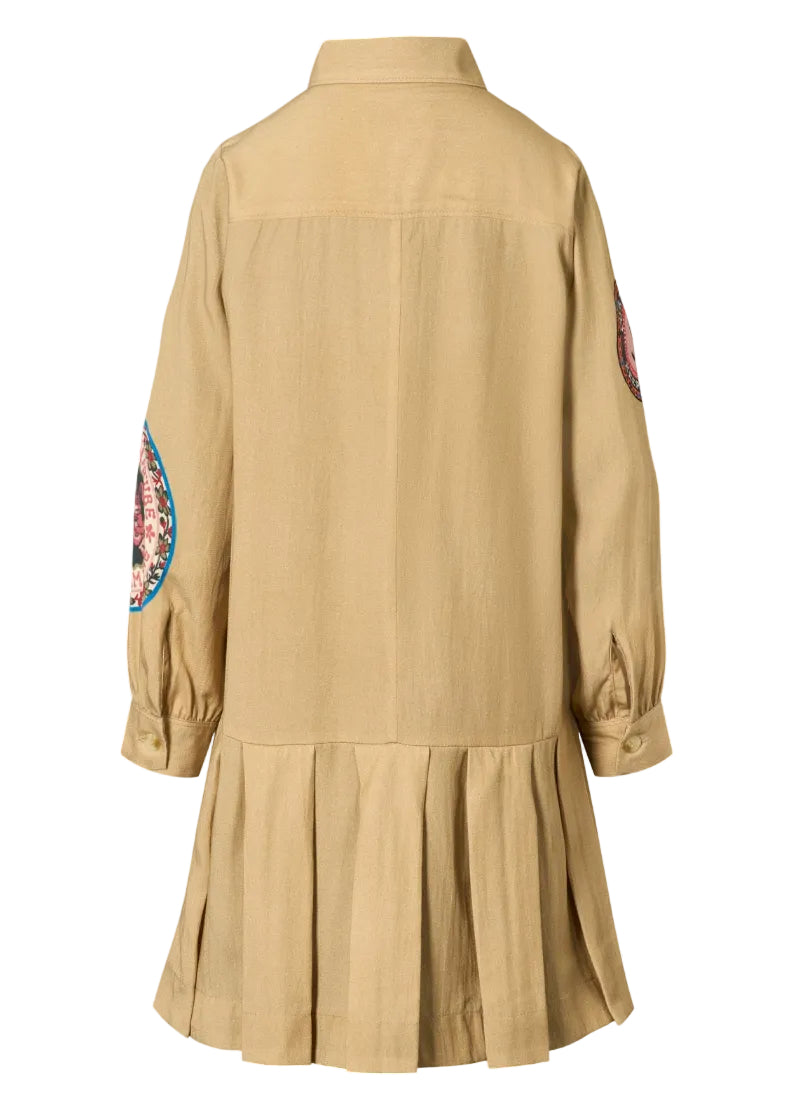A beige long-sleeve shirt dress with a pleated skirt hem, featuring circular embroidered patches on both upper sleeves.