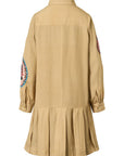 A beige long-sleeve shirt dress with a pleated skirt hem, featuring circular embroidered patches on both upper sleeves.