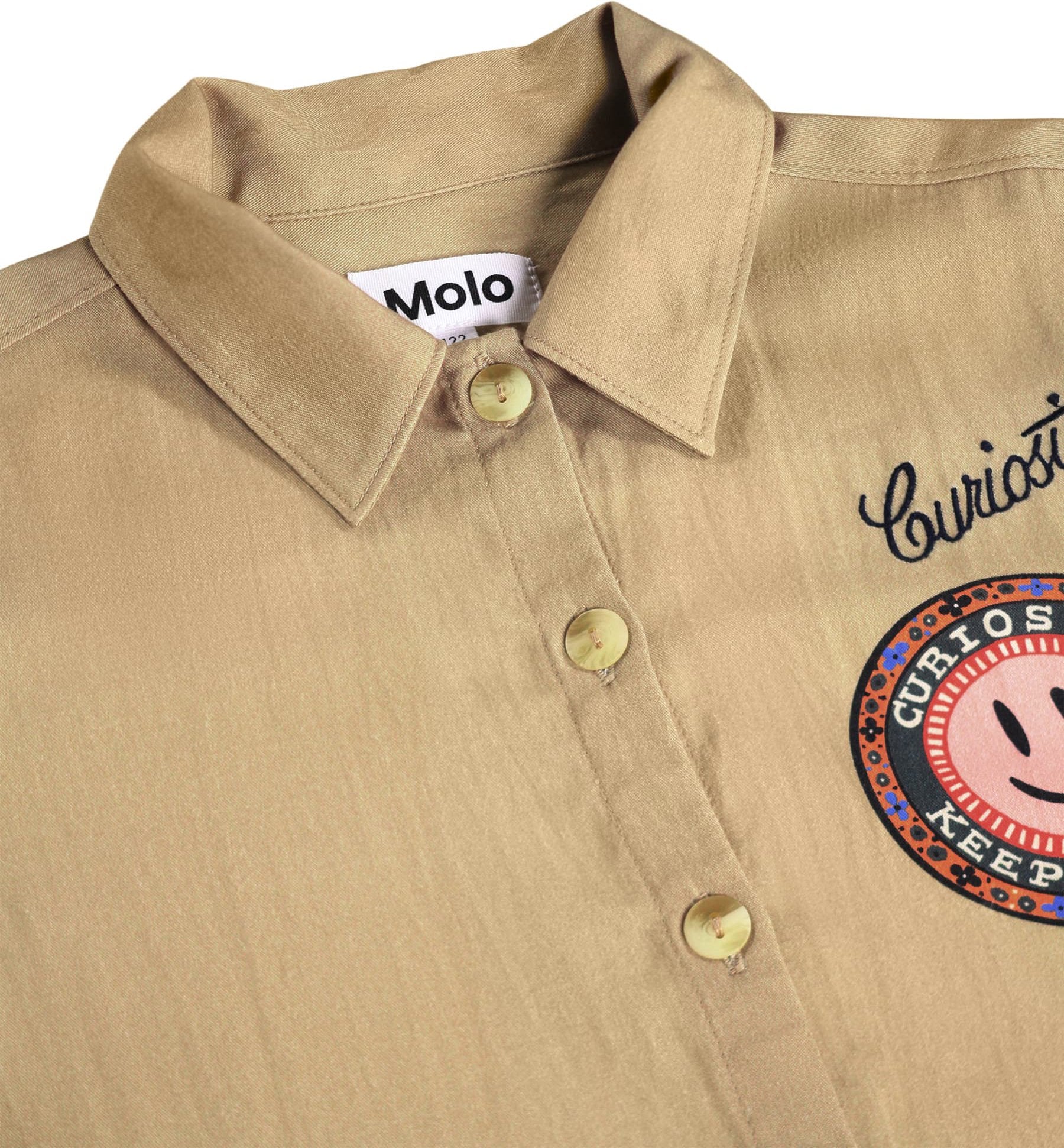 Close-up of a beige button-up shirt with a collar, showing the Molo brand label inside the neck, decorative script embroidery on the chest, and a circular patch with a smiley face.