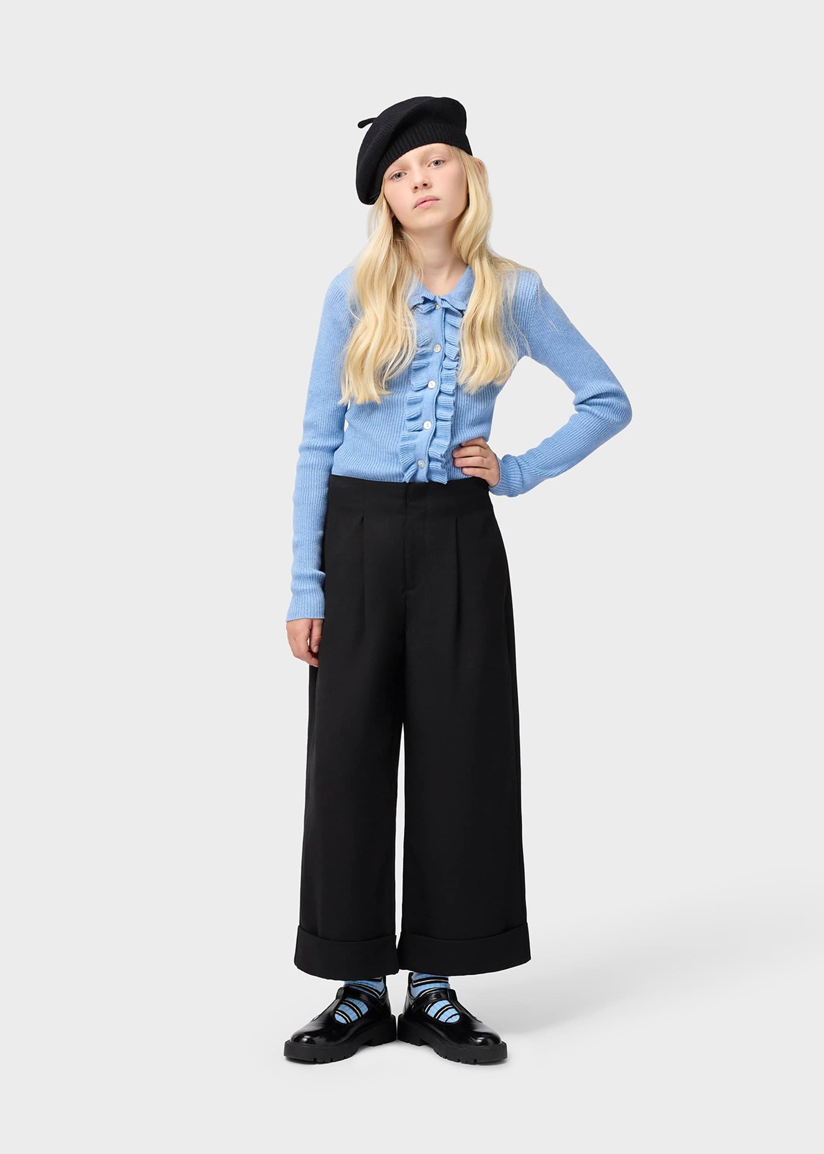 Person wearing a blue cardigan, black beret, and black wide-leg pants on a white background