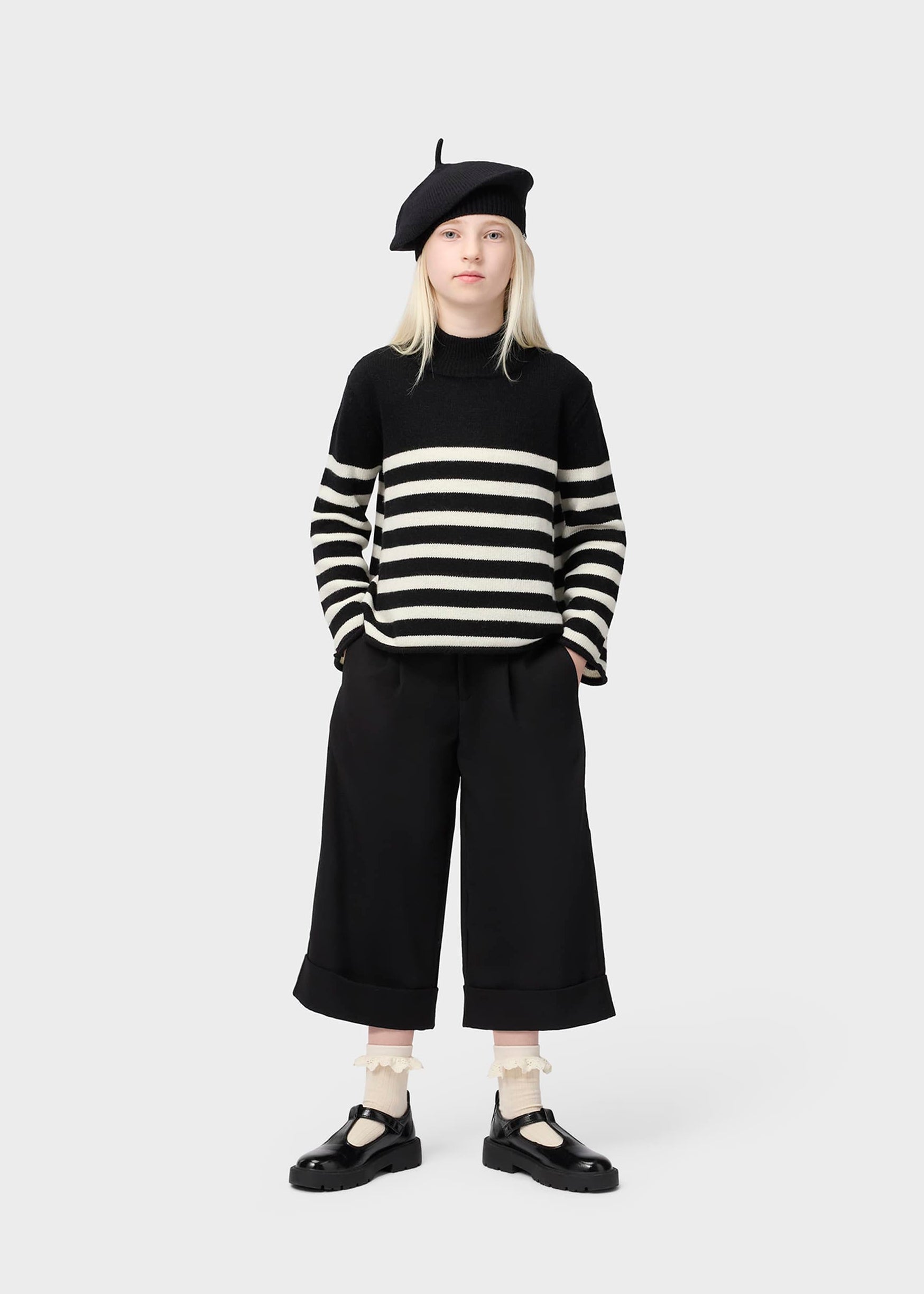 Person wearing a black and white striped sweater, black beret, and black pants on a white background