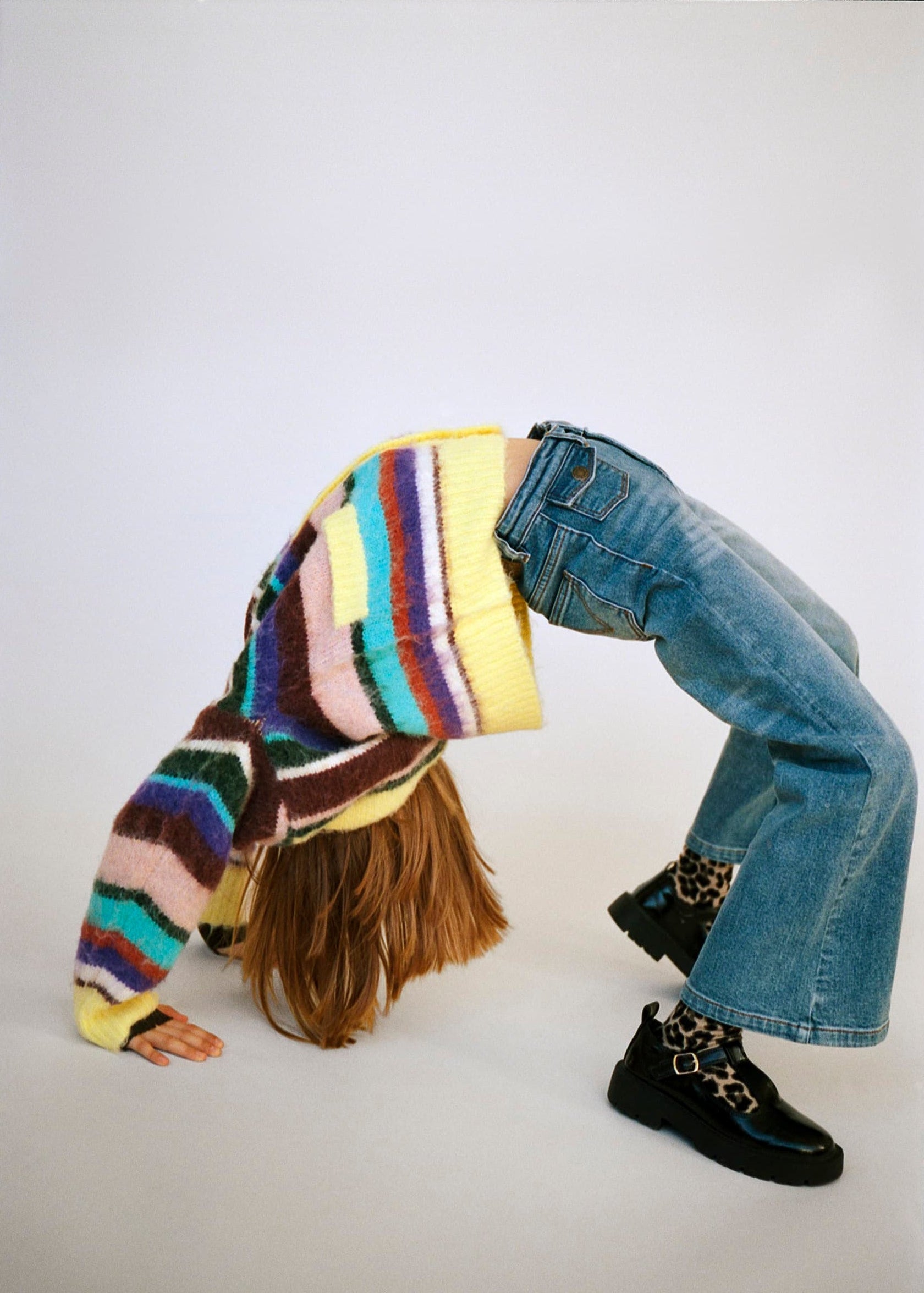 Person wearing a colorful striped sweater and blue jeans on a white background