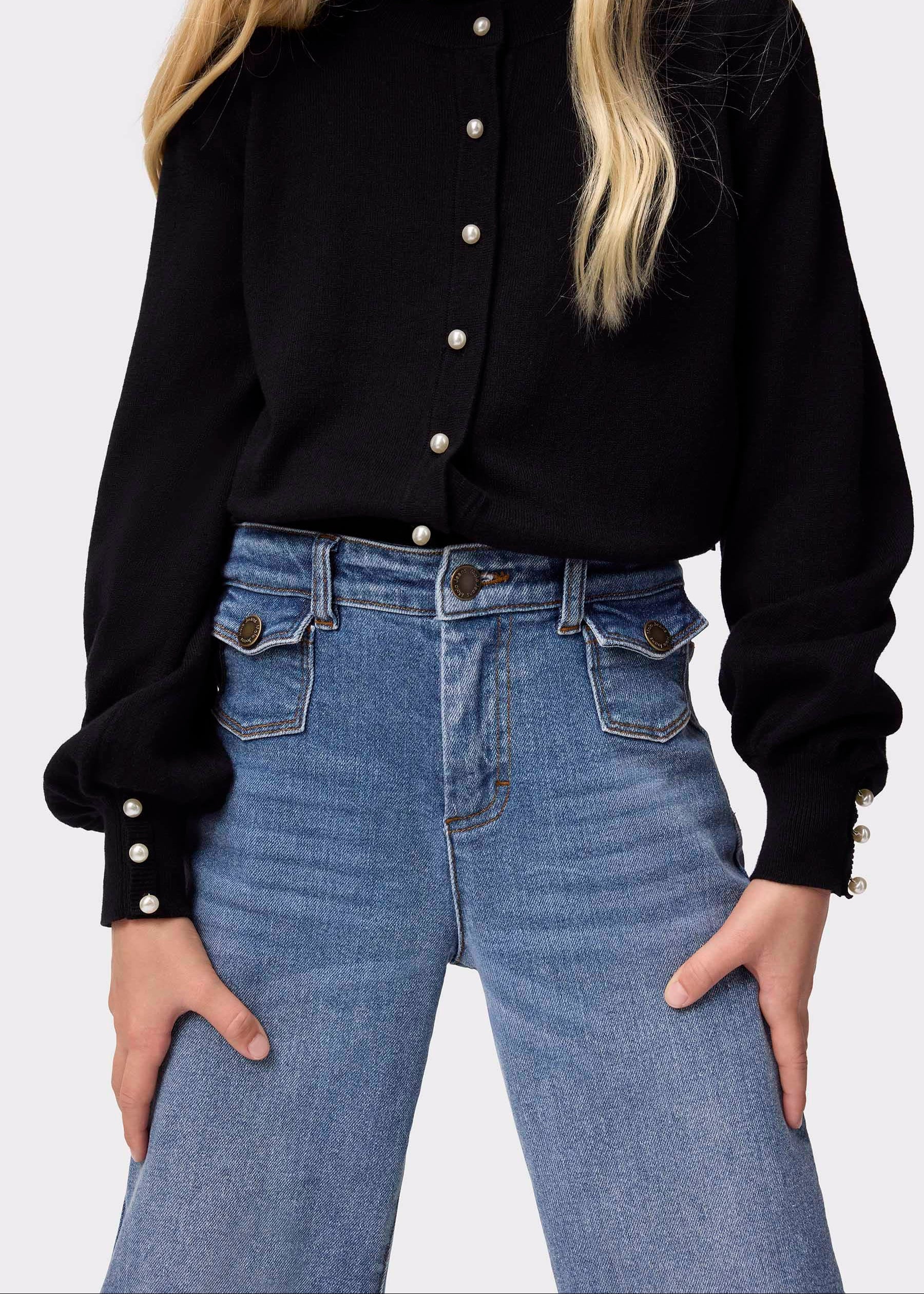 Person wearing a black blouse with pearl buttons and blue jeans on a white background