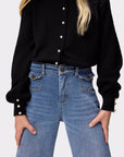 Person wearing a black blouse with pearl buttons and blue jeans on a white background