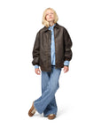 Person wearing a brown leather jacket, blue shirt, and jeans on a white background