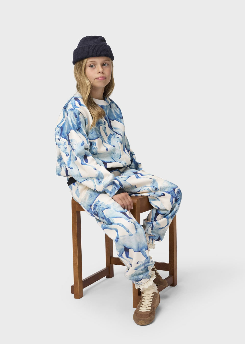 Person wearing a blue and white patterned outfit sitting on a wooden stool against a white background