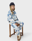Person wearing a blue and white patterned outfit sitting on a wooden stool against a white background