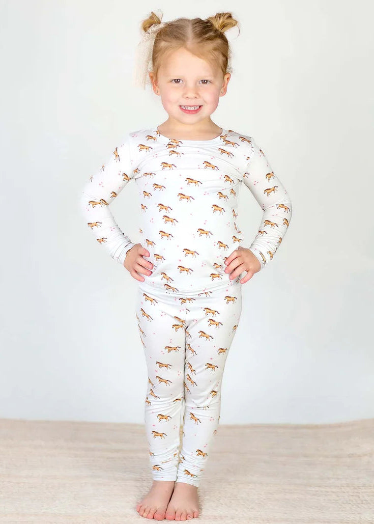 Young girl wearing a white pajama set with animal prints on a plain background