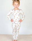 Young girl wearing a white pajama set with animal prints on a plain background