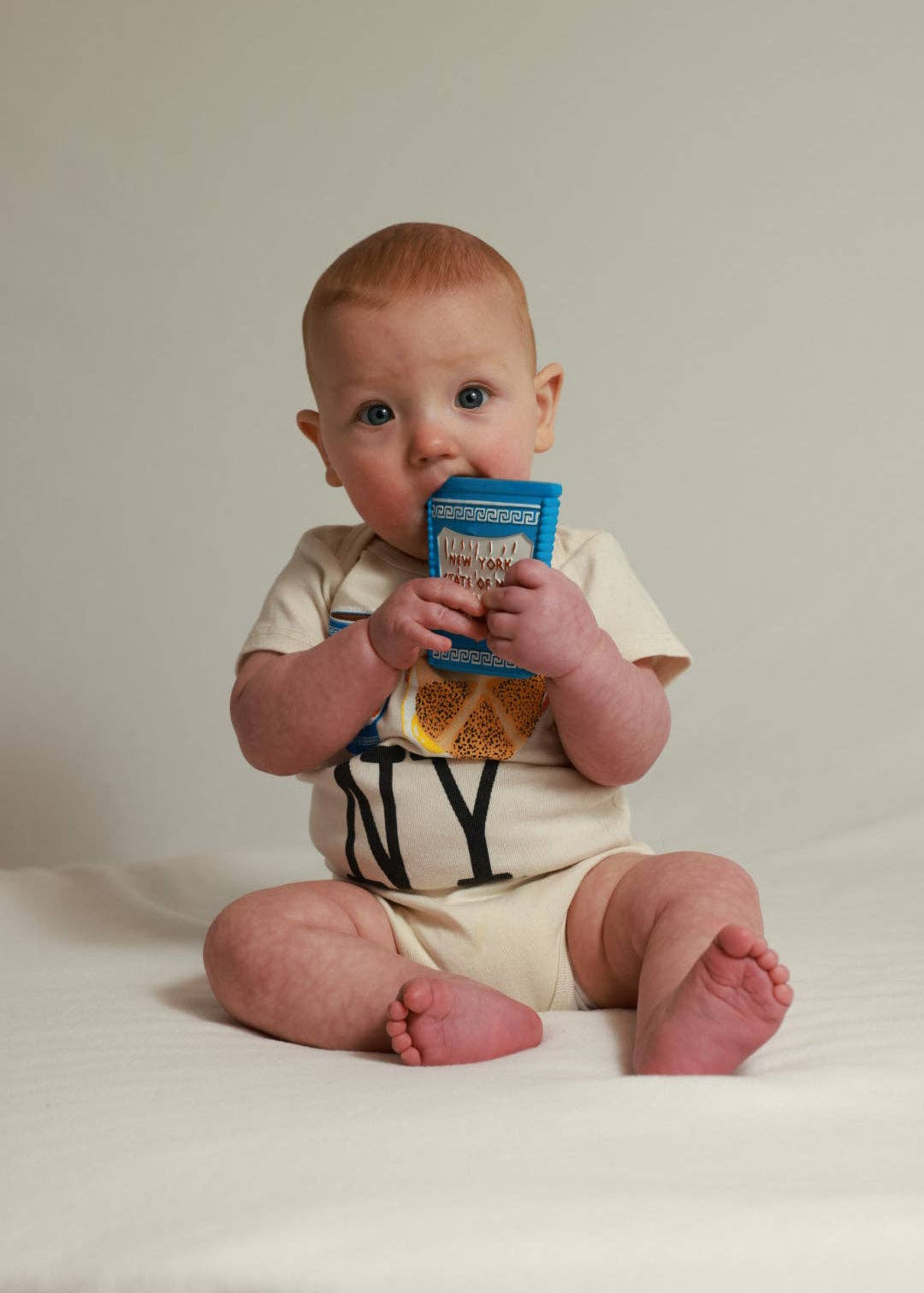 Baby sitting on a white surface holding a blue container.
