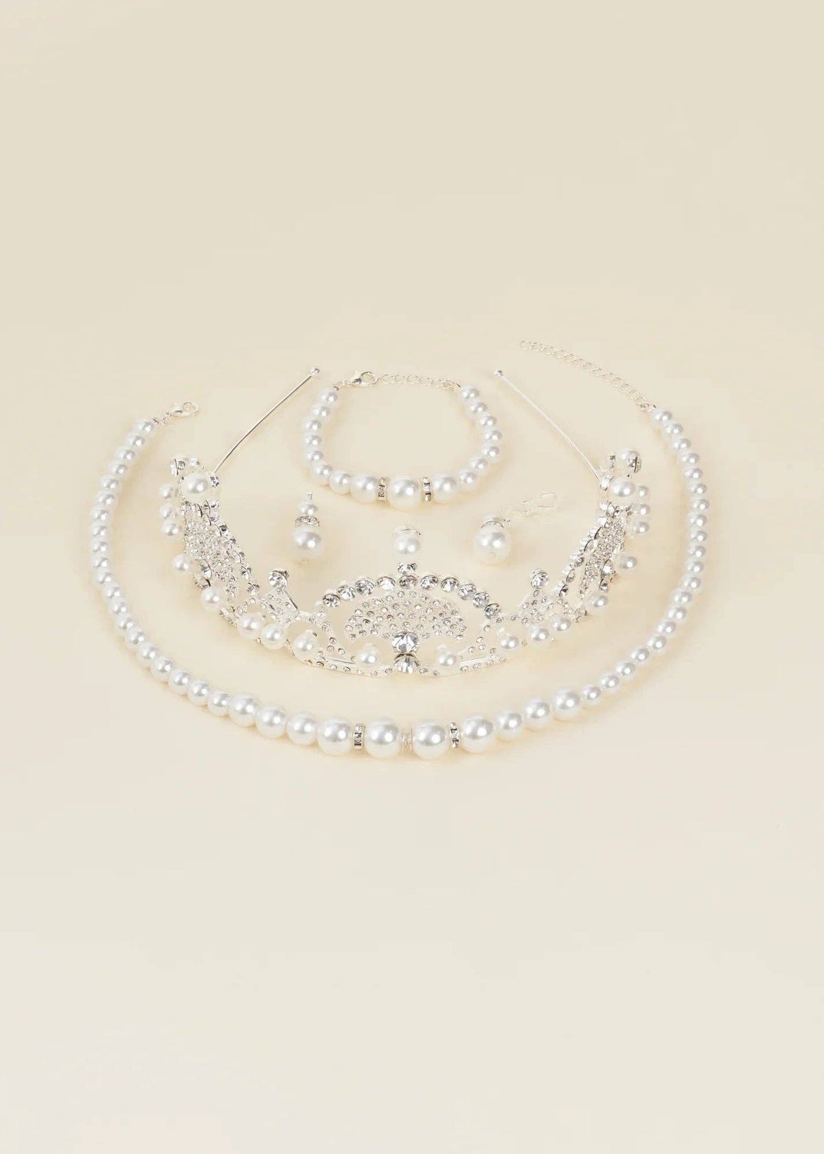 A silver and pearl bridal jewelry set featuring a tiara, collar necklace, bracelet, and earrings, arranged on a solid cream background.