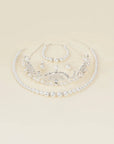 A silver and pearl bridal jewelry set featuring a tiara, collar necklace, bracelet, and earrings, arranged on a solid cream background.