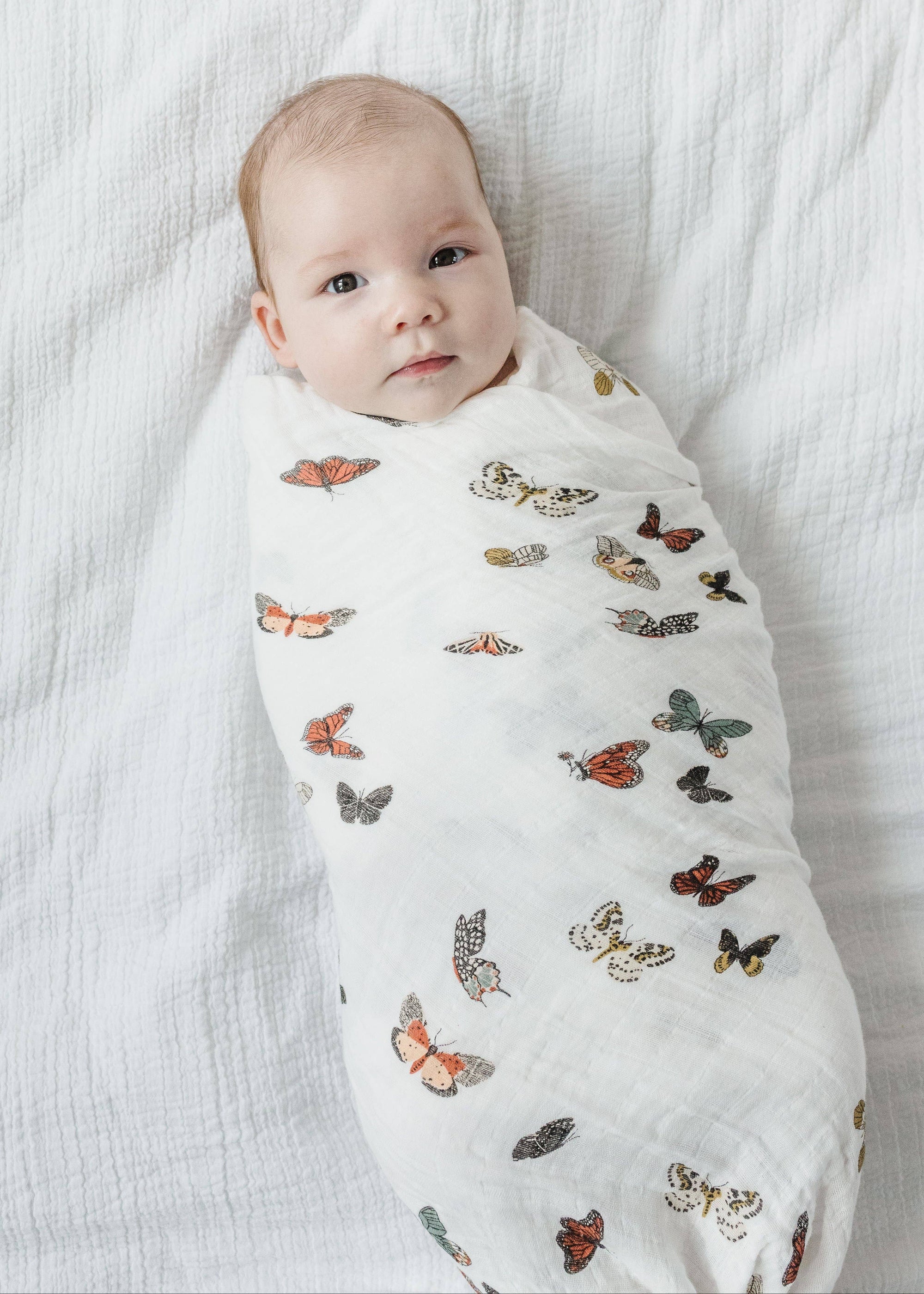 Baby wrapped in a butterfly-patterned swaddle on a white blanket