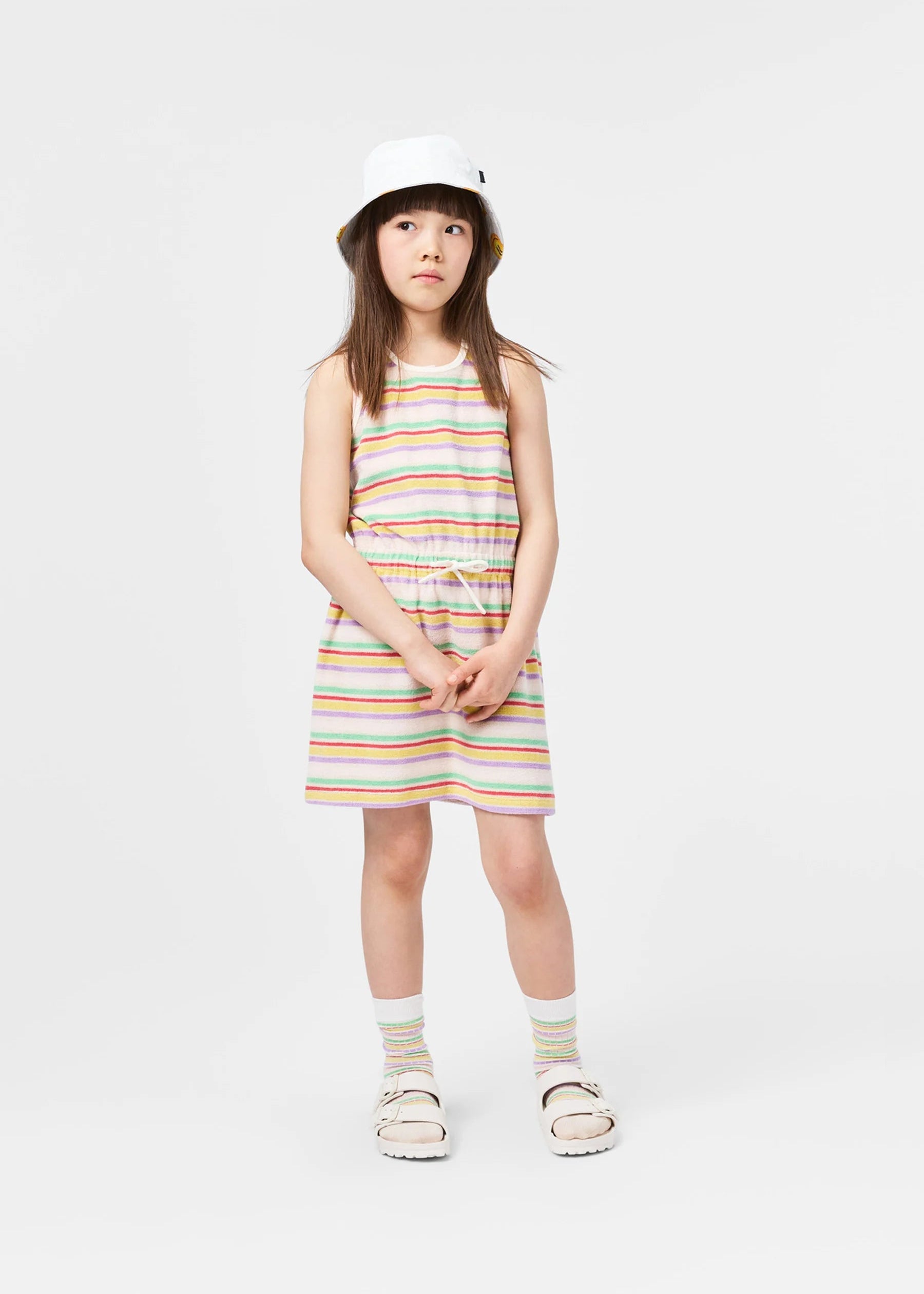 Young girl wearing a striped dress and bucket hat on a white background