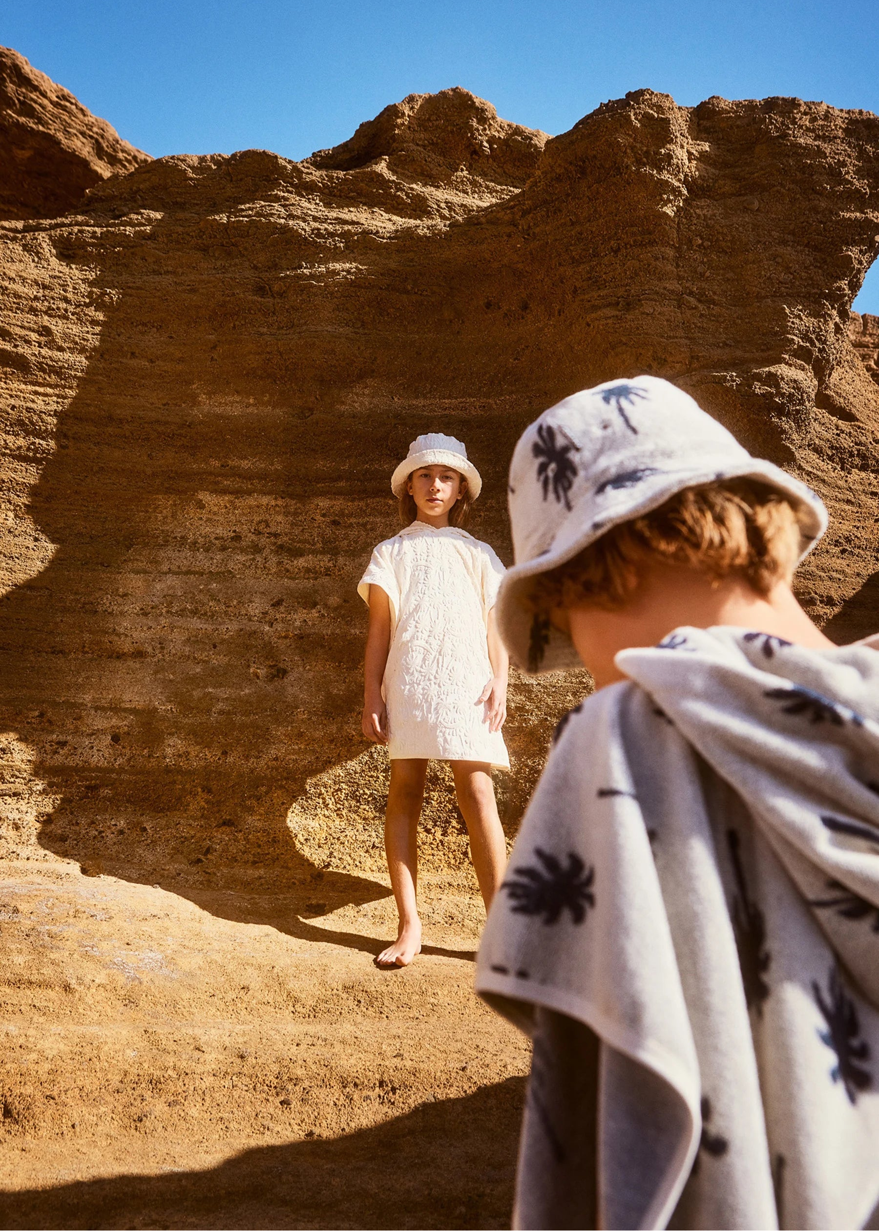 Two children in hats standing in a desert landscape with rocky formations.