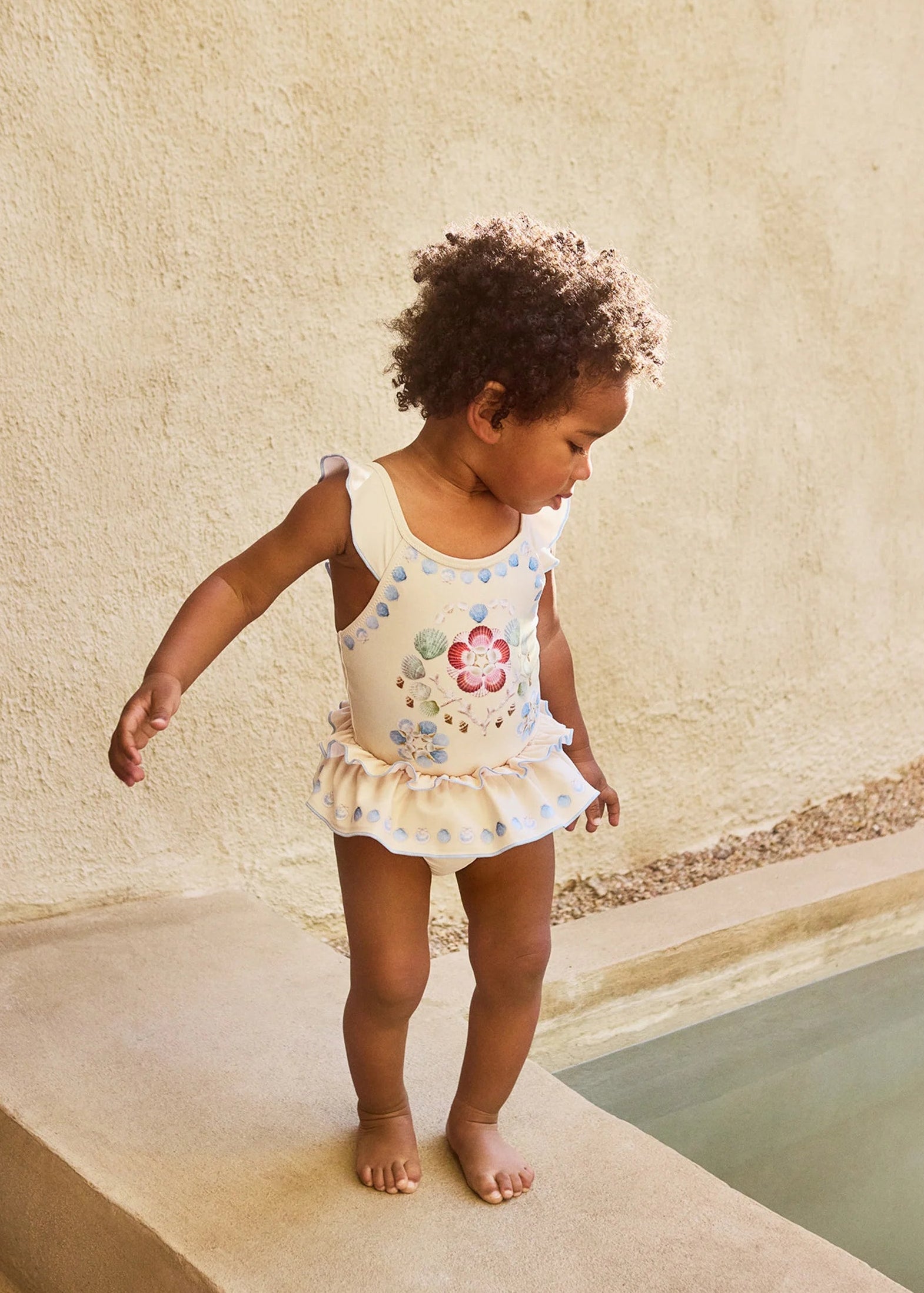 Child in a floral swimsuit standing by a poolside.