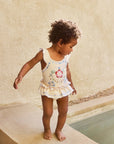 Child in a floral swimsuit standing by a poolside.