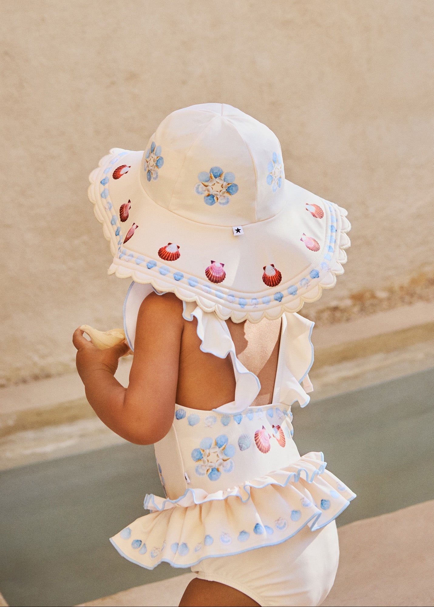 Child wearing a white sun hat and dress with floral patterns on a sandy background